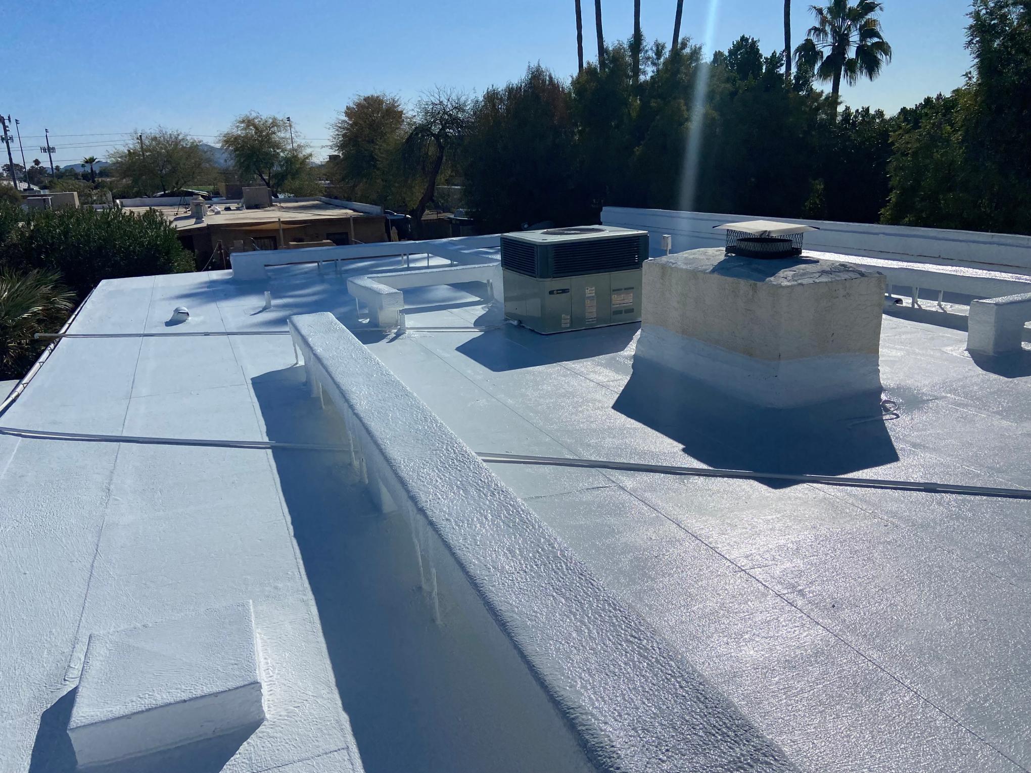 Completed white foam roof coating on a low slope Arizona home, with parapet walls, a rooftop air conditioning unit and a coated chimney