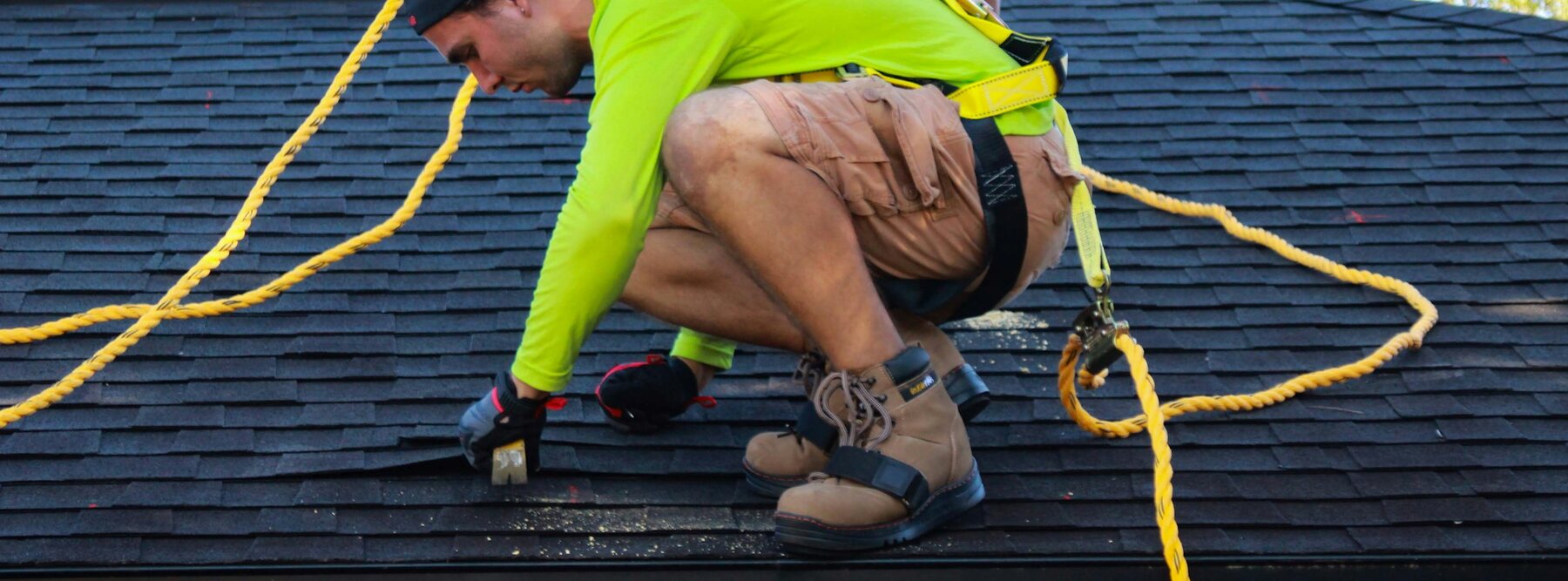 Roofer safely harnessed while repairing shingles after storm damage