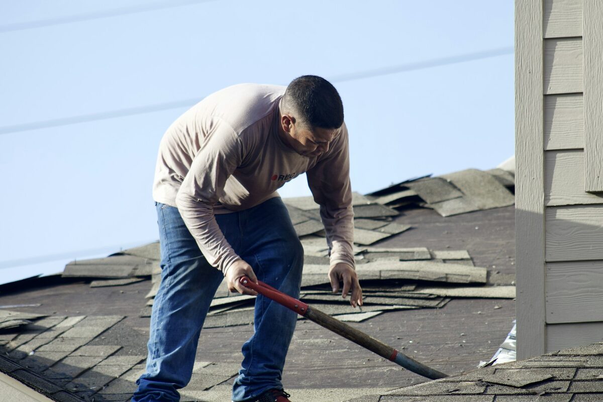 Roofer stripping damaged asphalt shingles during a repair